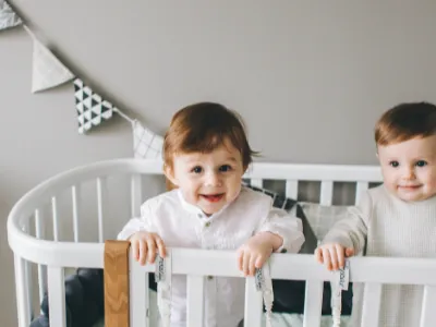 twee kinderen met witte kleding en bruin haar in de wieg