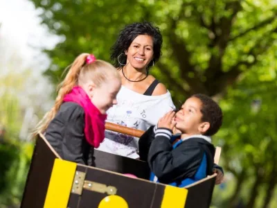 Lachende vrouw met twee kinderen in een kartonnen doos buiten, zonnige dag.