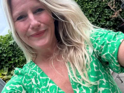 Vrouw met krullend bruin haar, gekleed in een geel shirt, glimlachend naar de camera.