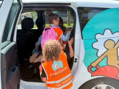 Twee kinderen dragen oranje hesjes met het logo van Kindercentrum De Bloeiboei terwijl ze de auto instappen.