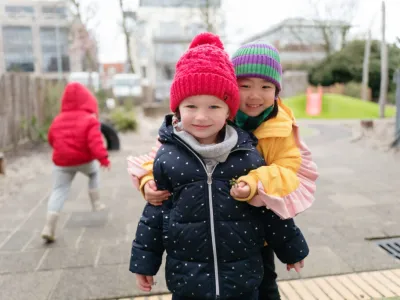 Twee meisjes poseren knuffelend voor de foto op het buitenplein van de internationale kinderopvang