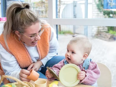 Pedagogisch medewerker en kind spelen aan tafel met bord