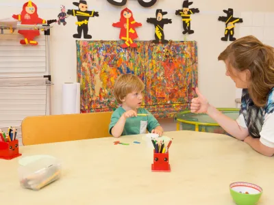 Kind en pedagogisch aan tafel. We streven ernaar onze tarieven zo laag mogelijk te houden.