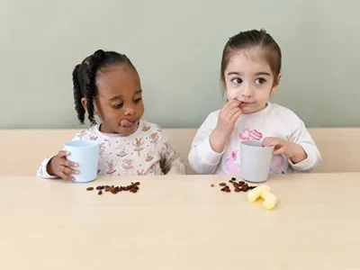 Twee peuters eten rozijntjes op de peuteropvang.