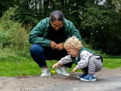 pedagogisch professional kijkt met een spelend kind naar een paardenbloem