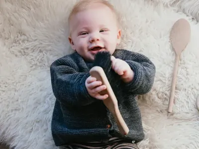 Baby ligt lachend op de grond met speelgoed in handen