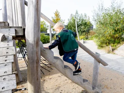 Jongetje klimt op trap in het buiten-klimhuisje op de kinderopvang
